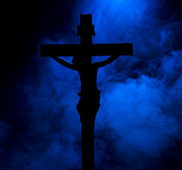 A small statue of Jesus Christ on the cross, in silhouette, against a smoky background