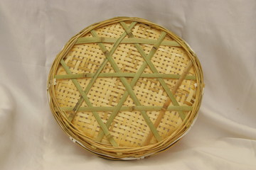 The bottom of a handmade round bamboo sieve. Green woven materials on tray