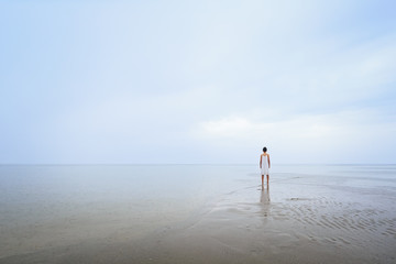 Lone girl on a beach in the rain wearing a white dress. Looking into the distance. Copy Space, room for text or inspirational quote