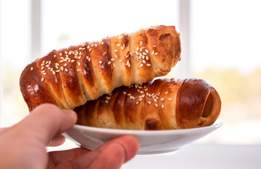 sausage in the dough on a plate, in hand, against a window
