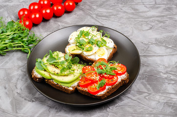 A variety of mini sandwiches with cream cheese and vegetables on a black plate.