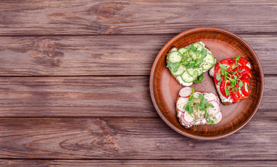 A variety of mini sandwiches with cream cheese and vegetables in a clay plate.