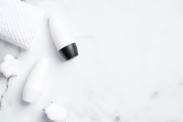 Roll-on deodorant bottles with cotton flowers and towel on marble background. Flat lay, top view. Underarm skin care, sweat protection concept