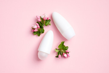 Blank deodorant bottles and flowers on pink background. Flat lay, top view. Antiperspirant packaging mockups, underarm skin care, sweat protection concept