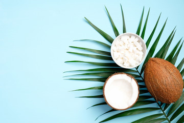Obraz na płótnie Canvas Flat lay composition with coconut and tropical palm leaf on blue background. Concept of healthy eating or organic SPA cosmetic ingredients. Summer background.