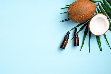 Coconut aromatherapy oil with coconut and palm leaf on blue background. SPA organic cosmetic product, body care concept. Flat lay, top view