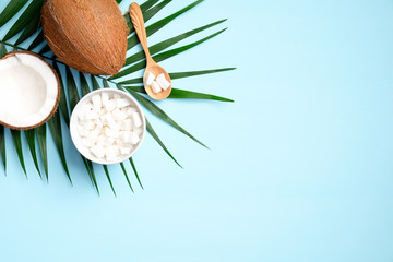 Flat lay composition with coconut and tropical palm leaf on blue background. Concept of healthy eating or organic SPA cosmetic ingredients. Summer background.