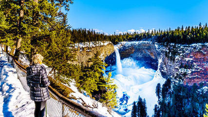 Senior woman viewing Helmcken Falls on the Murtle River in winter with the spectacular ice and snow...
