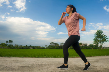 outdoors jogging workout - young happy and dedicated Asian Korean woman running at beautiful ccountryside road under a blue sky on enjoying fitness and cardio activity