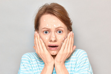 Portrait of unhappy sad girl with white drops of face cream on skin