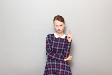 Portrait of serious focused young woman pointing up with index finger