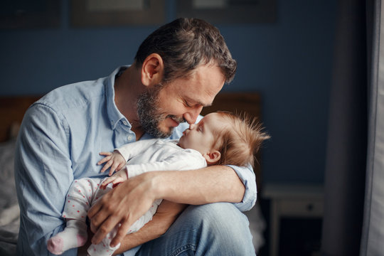 Middle age Caucasian father kissing sleeping newborn baby girl. Parent holding rocking child daughter son in hands. Authentic lifestyle parenting fatherhood moments. Single dad family home life.