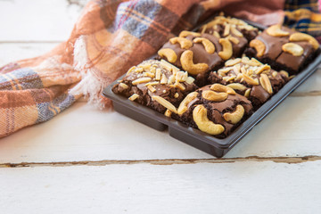 Close up brownie with cashew nuts on top in a brown plastic pack on white wooden table with pattern fabric for send to customer.