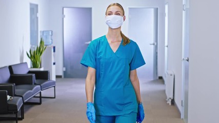 Charismatic lady nurse after the surgery intervention she walking in the corridor hospital with a protective mask in front of the camera