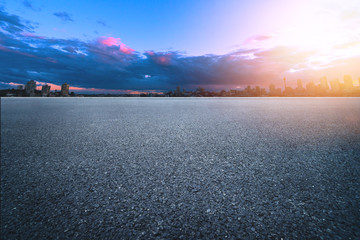 Asphalt road at sunset with city background. Empty asphalt highway and building with nice sky...
