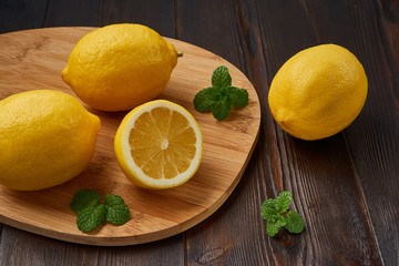 Several juicy yellow lemons with mint leaves on a cutting board