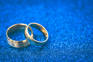 Gold wedding rings of bride and groom on dark blue gliter