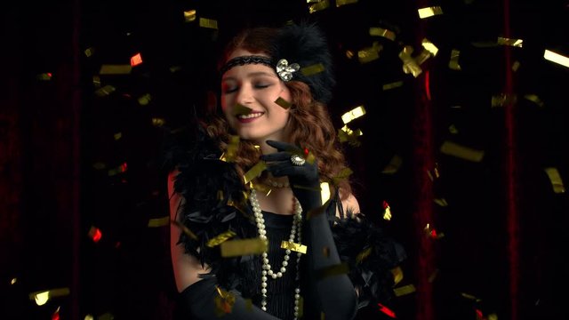 Portrait of vintage styled woman dressed in Great Gatsby era dancing under confetti rain on velours background. Roaring twenties, retro, party, fashion concept