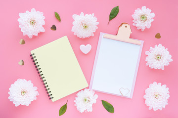 Mock up pink clipboard, yellow notepad on a spring heart and pink flowers on a pink background. Flat layout, top view..