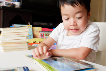 An Asian boy is reading a book on a white table.