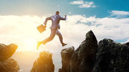 Back view of black businessman jumping over mountain stones