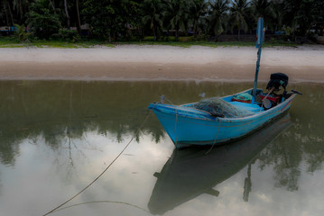 Small blue fishing boat sitting in tidal bay with reflection in water