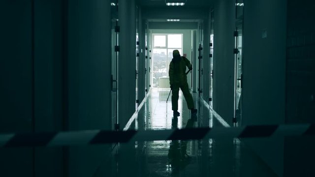 Inspector in a hazmat suit is disinfecting a dark corridor