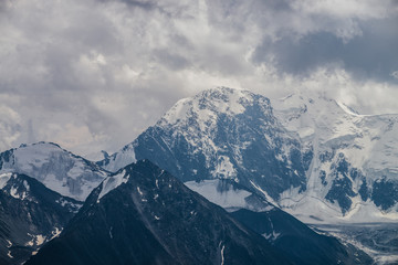 Awesome landscape with huge glacial mountains in bad cloudy weather. Low stormy clouds touch top of snowy mountain with glaciers. Storm is coming due to mountains. Gloomy overcast atmospheric scenery.