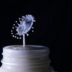 White drops colliding into an umbrella of splashes in a glass.