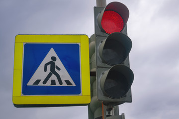 Traffic light with a burning red light on a background of cloudy sky.