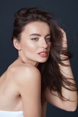 Fototapeta premium Beautiful Girl. Young Woman Touching Hair Portrait. Blue-Eyed Brunette With Smooth Perfect Skin And Natural Makeup On Black Background. Naked Shoulders Model Looking Away.