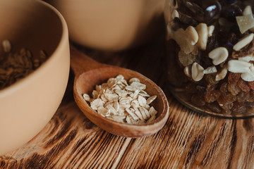 Oatmeal in a wooden spoon on a wooden background and dried fruit in a glass jar. The concept of a healthy diet and healthy lifestyle.