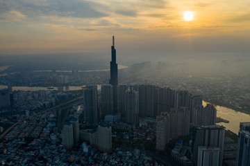 Sunrise drone shot of misty Ho Chi Minh City urban landcape with high rise tower in silhouette and view of Saigon River