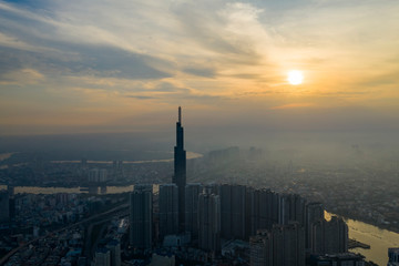 Fototapeta premium Sunrise drone shot of misty Ho Chi Minh City urban landcape with high rise tower in silhouette and view of river