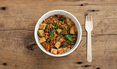 Thai basil pork stir fried  with rice in food paper box on wooden table, takeaway street food, top view