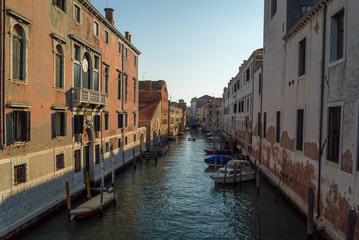 Fototapeta na wymiar A scenic view of a beautiful Venetian canal on a warm sunny day with colourful houses and boats running along the water in the town of Venice, Italy