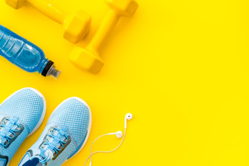 Fitness accessories. Dumbbells and sneakers on yellow table top view copy space