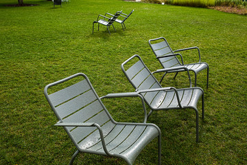 Empty wet plastic chairs stand on the green grass after the rain.