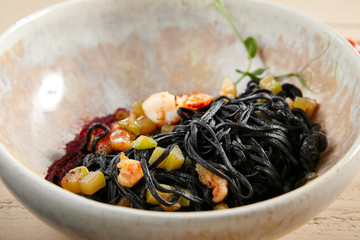 Black spaghetti with shrimp and zucchini in beige bowl