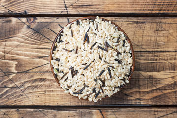 Raw wild rice in a wooden bowl. Raw rice grits on a wooden background. Copy space.