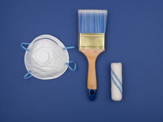 Respirator, paint brush and roller on a blue background.
