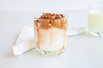 Home made Dalgona whipped chocolate in a cup on white table with a cup of milk background.