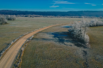 Aerial panorama of cold winter fire road on Planinsko polje field in Slovenia, Europe. Picturesque cold winter panorama without snow of fields and meadows lit by winter sun.