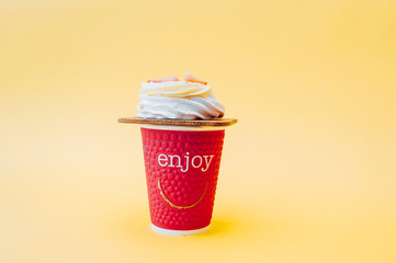 white pastry souffle with cream and fresh strawberries and a red paper Cup with the words Enjoy on a soft yellow background.