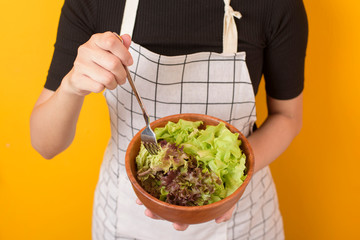 Beautiful healthy woman is eating vegetables on yellow background