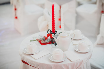 Romantic gala dinner setting with red and white candles on white tablecloth and napkins. Romantic white tea table with candles.