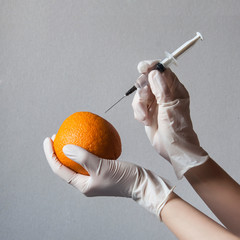 Research experiments with GMOs on fruit. A person injects a GMO injection into an orange