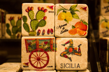 colored images reproduced on cube-shaped stones promoting the Sicily region in Italy 
depicting citrus fruits, lemons, oranges, cactuses typical Sicilian cart and 
female head with three folded legs c
