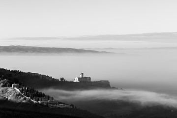 Fototapeta na wymiar An epic view of St.Francis church in Assisi town (Umbria) above a sea of fog at dawn