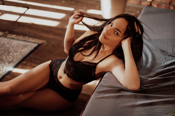 Young and sensual woman sitting on the floor and leaning on the bed wearing lingerie, close-up portrait - obrazy, fototapety, plakaty